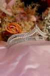 Silver bridal tiara with pearl strands, pavé rhinestone rails and starburst centre crystal on pink satin — Feriha Bridal
